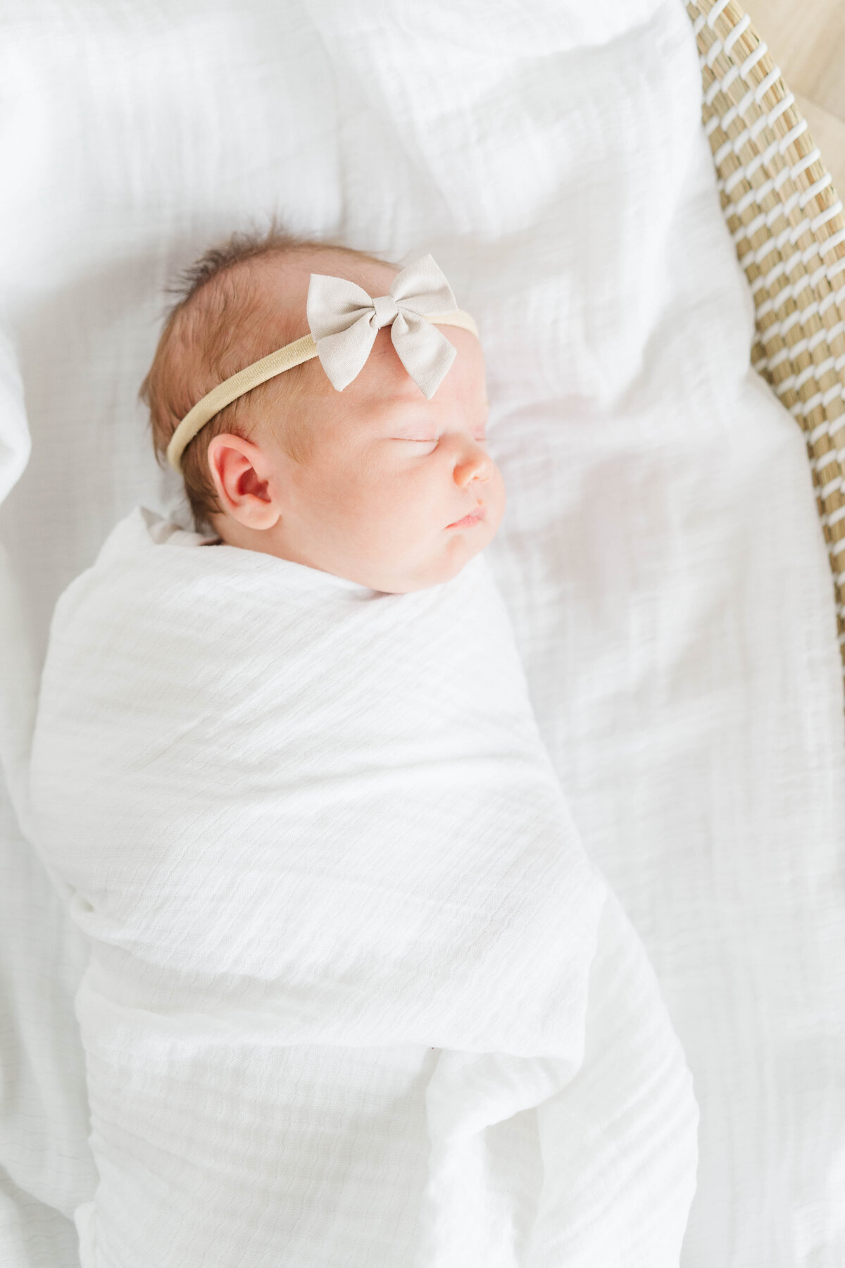 A sleeping newborn girl swaddled in soft fabric, wearing a delicate bow on her head