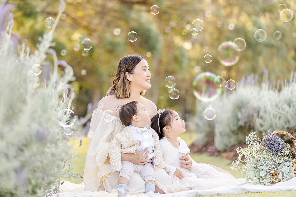 Asian mum holding two kids admiring bubble show in Brisbane.
