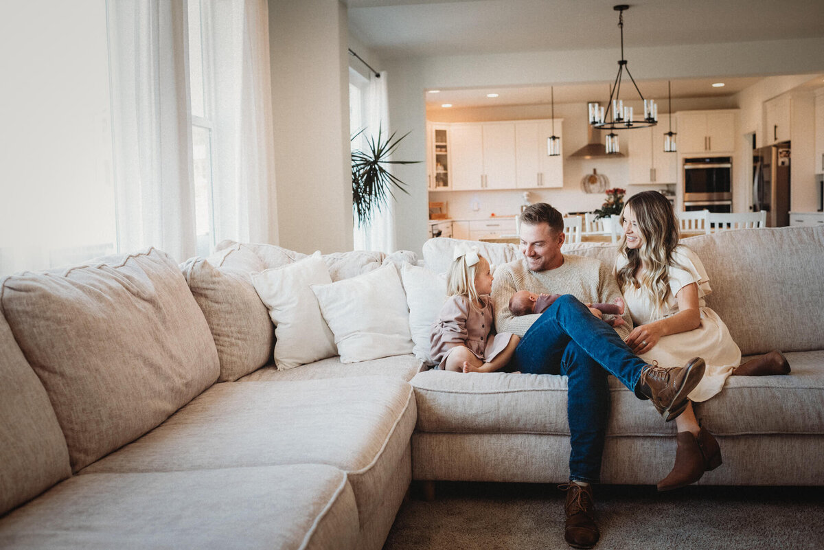 A family of four sit on a couch together with newborn baby