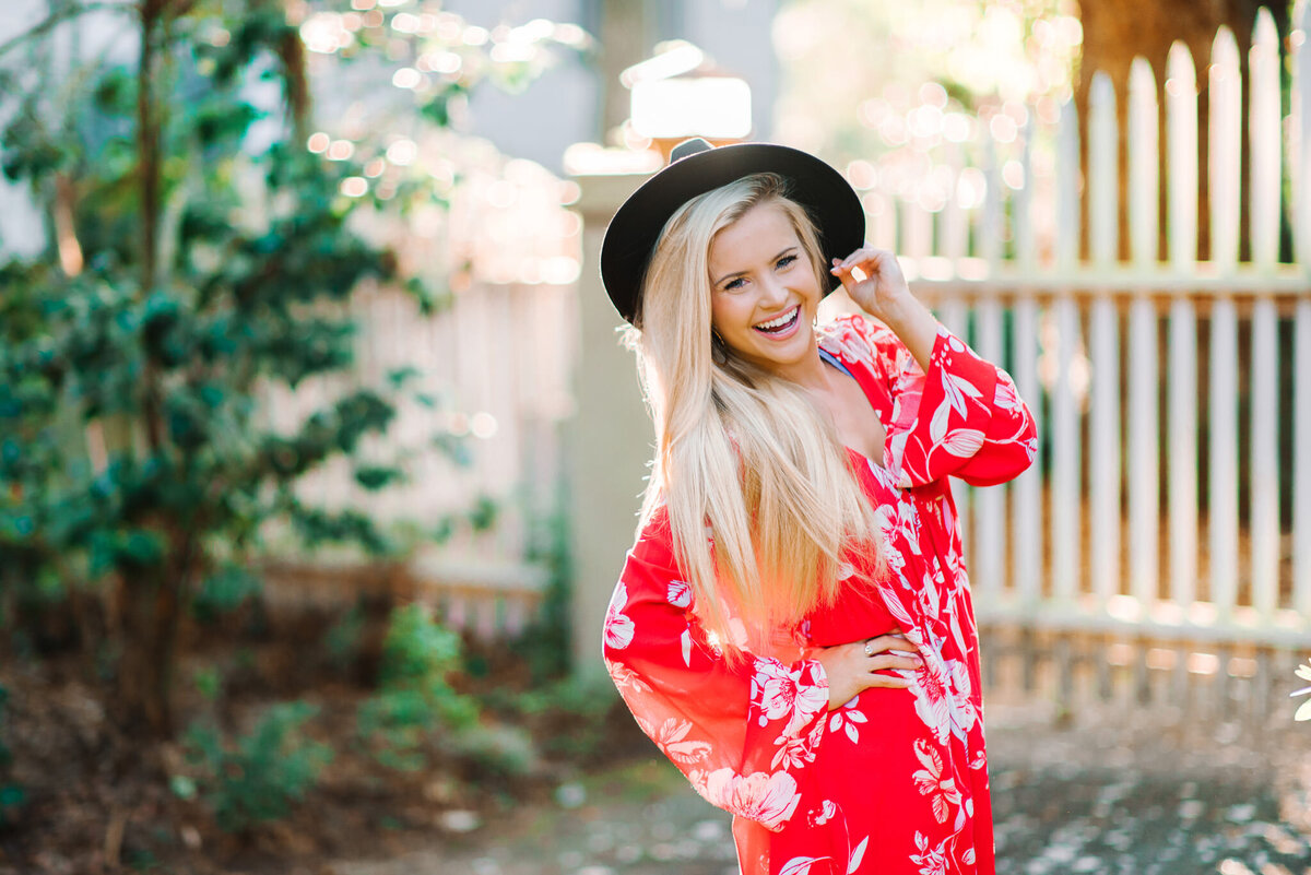 Teen girl in red top and wide-brim hat posing playfully in a lush garden in Charleston, SC