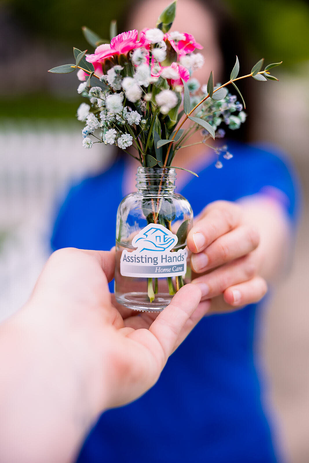Woman holding out a jar of flowers with home care agency logo