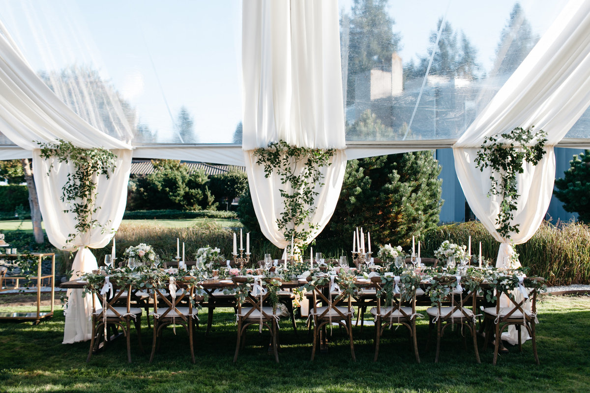 Romantic clear tent wedding reception with ceiling draping and greenery covering the tent legs