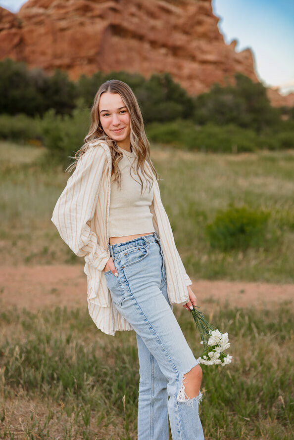 Girl in white shirt poses at Red Rocks Park with flowers in her hand.