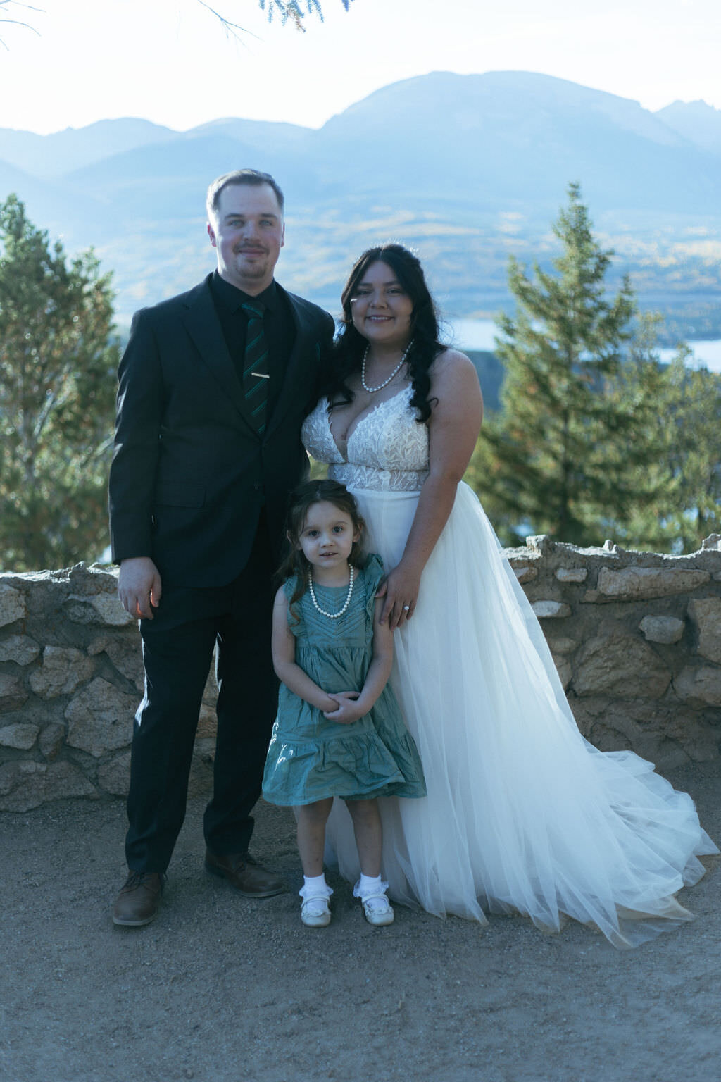 A newlywed couple smiling with a small child in front of them.