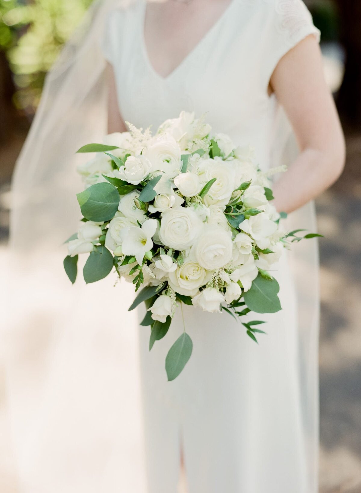 Spouse-to-be dressed in a white wedding dress holding a beautiful bouquet of white roses.