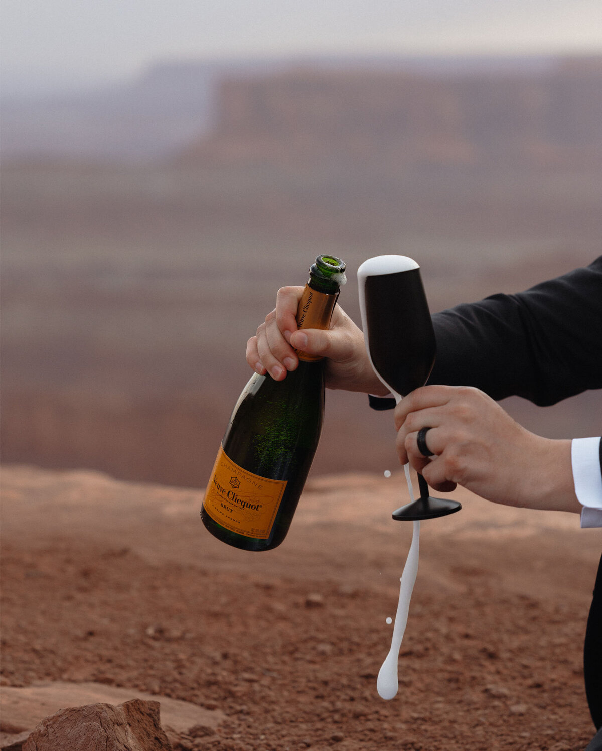 groom pours champagne as it overflows his glass after private elopement ceremony in Moab, Utah