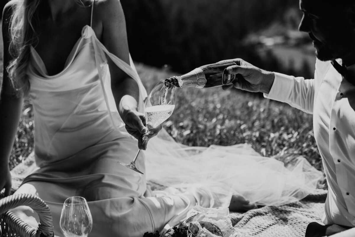 Close-up of couple pouring champagne into glasses on blanket
