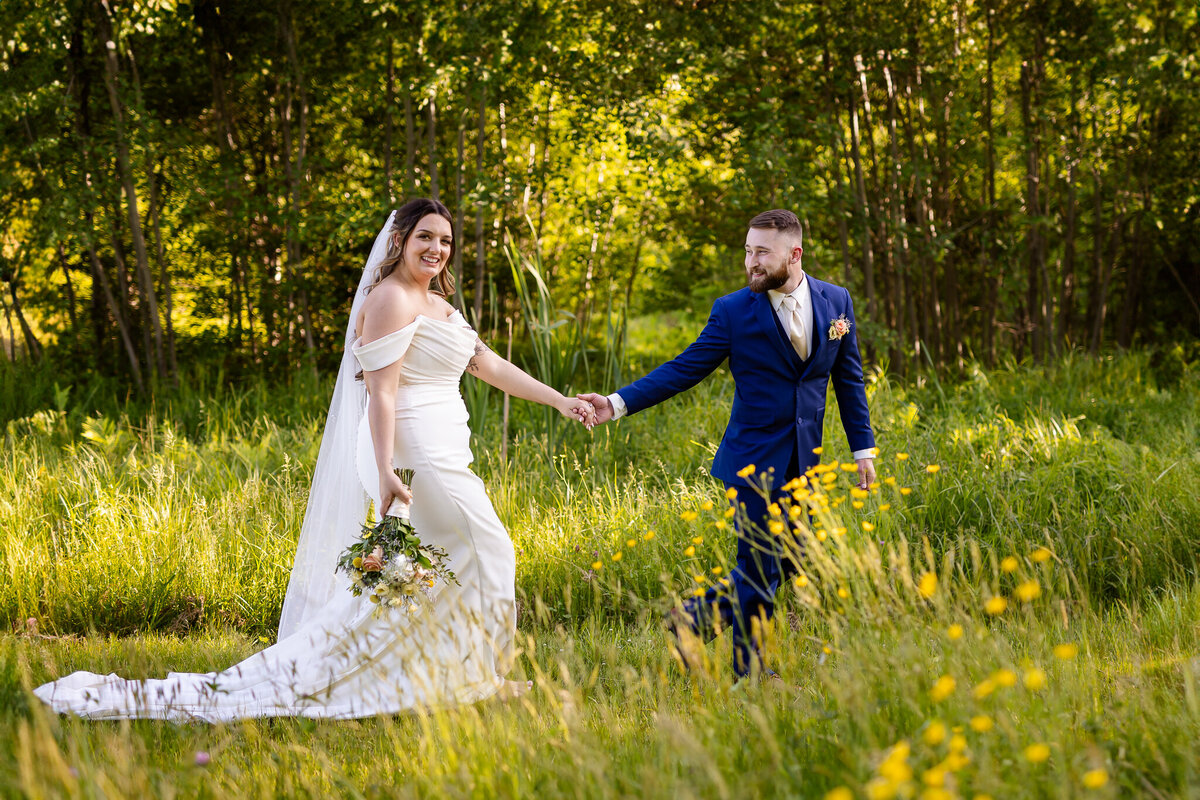groom leading bride through field in spring by NH Wedding Photographer Lisa Smith Photography