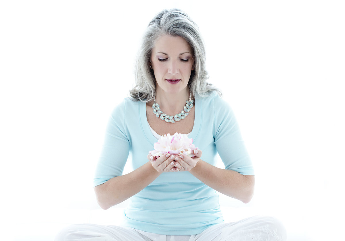 life  coach personal brand  photography  lady sitting on teh floor  meditating with  flower lotus in her hand  wearing a blue  top  backlight setting