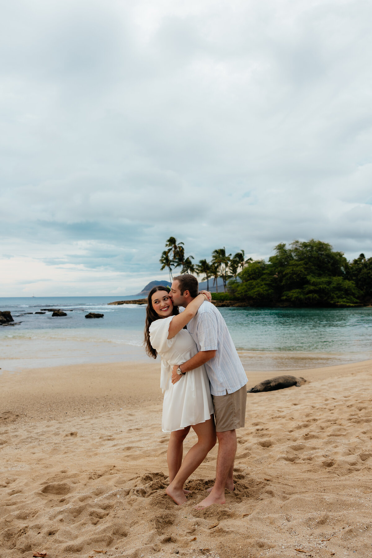Couple embracing on the beach in Oʻahu with palm trees and ocean views in the background during their romantic photoshoot at Paradise Beach Cove in Ko Olina