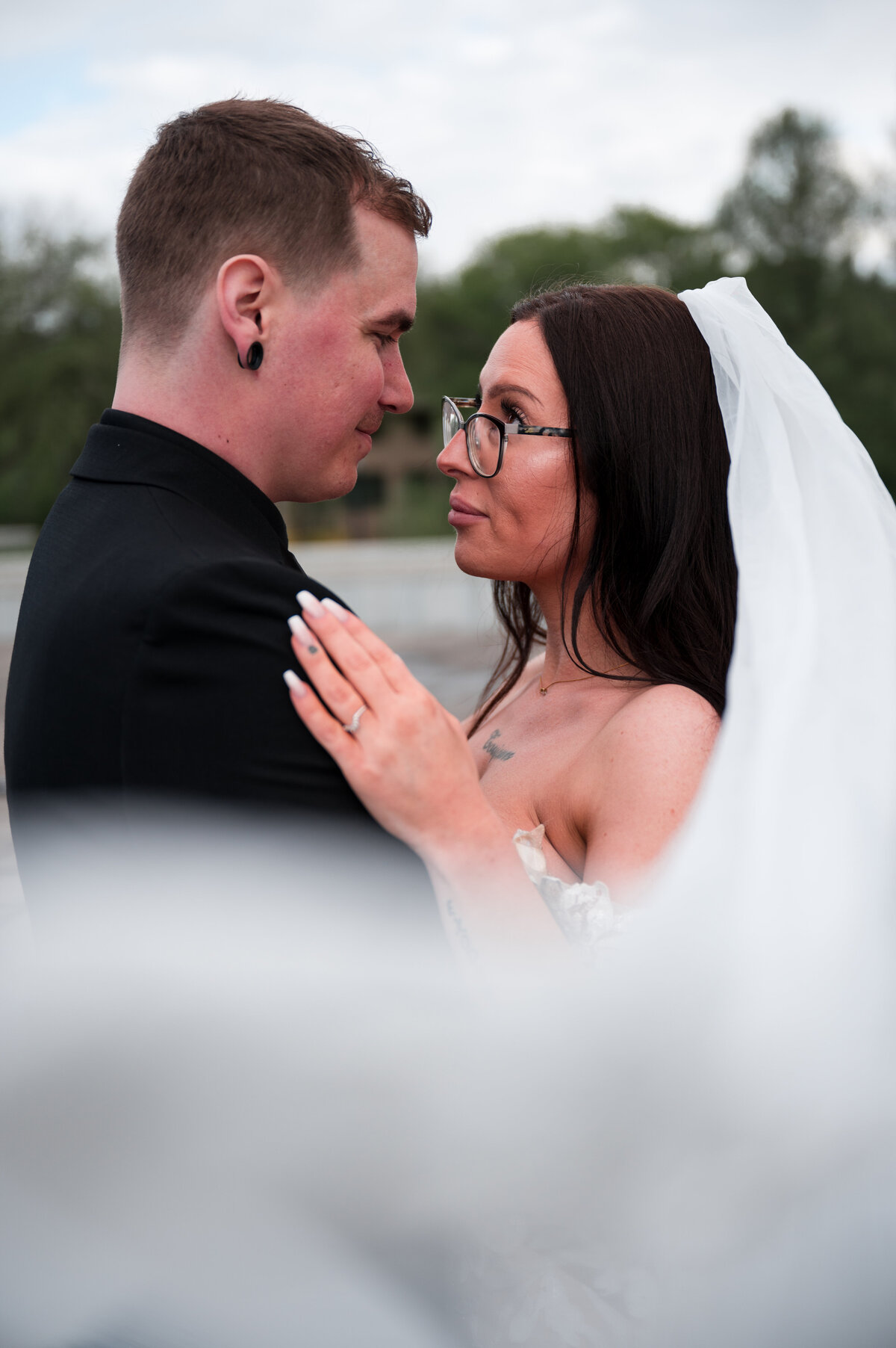 bride and groom stand facing each other, veil is swooped around them in romantic wedding portrait