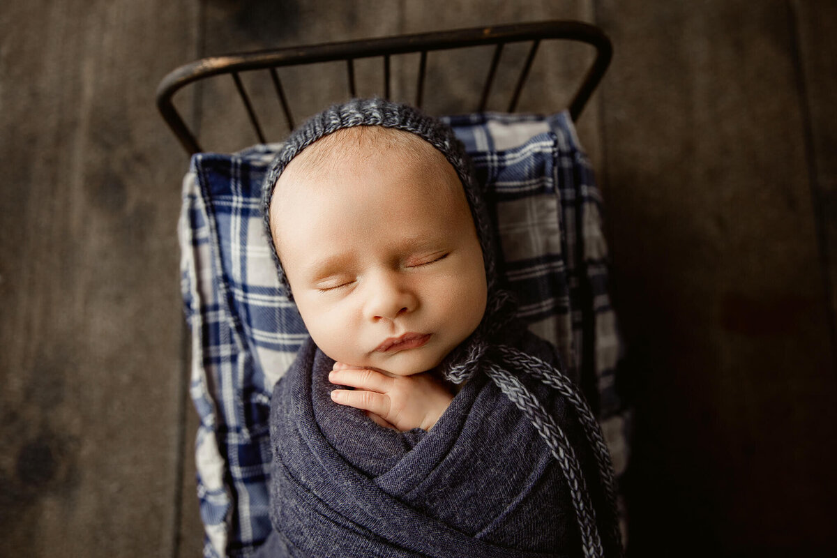 A peaceful newborn boy snoozing in a tiny bed, wrapped snugly in a soft blue blanket.