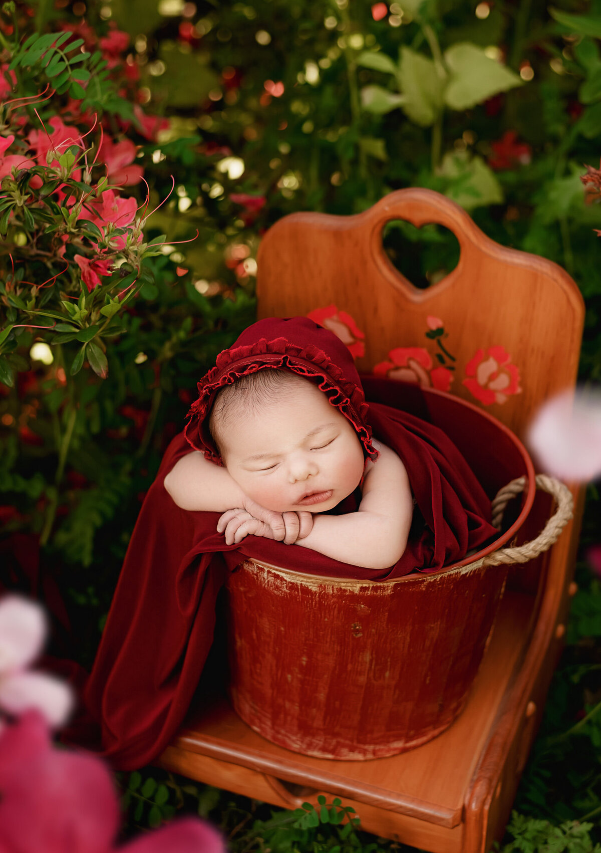 Outdoor photography session of infant girl  wearing a red hat in a bucket surrounded by flowers in  Vineland, Ontario.