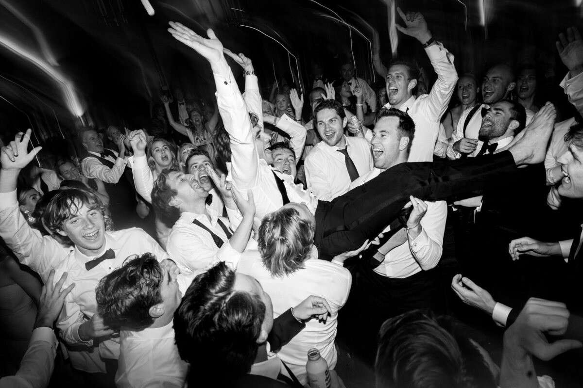 Black and white photo of the groom being carried by the groomsmen. 