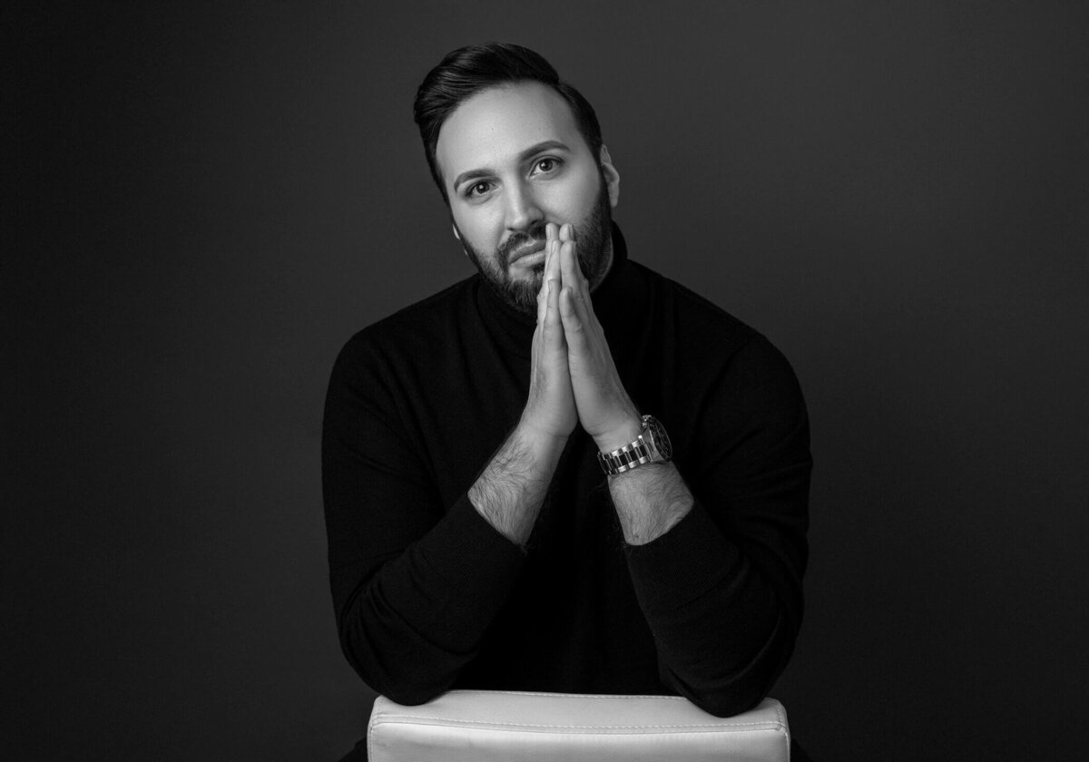 Black and white portrait of a bearded man in a turtleneck, hands together in thought.