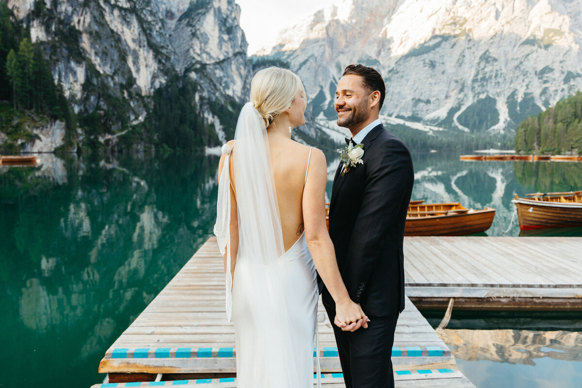Bride walking toward groom on wooden dock at lake