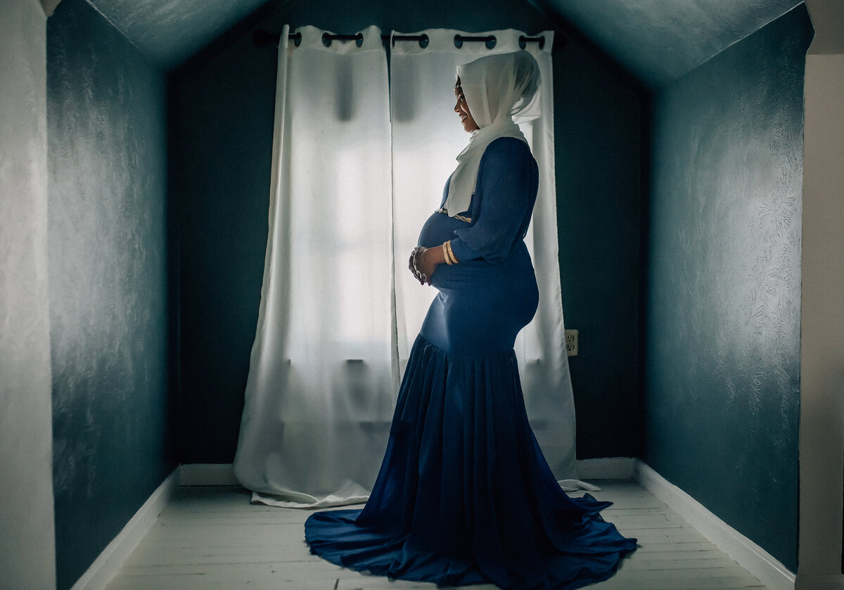 Maternity photograph of mom standing next to window holding belly.