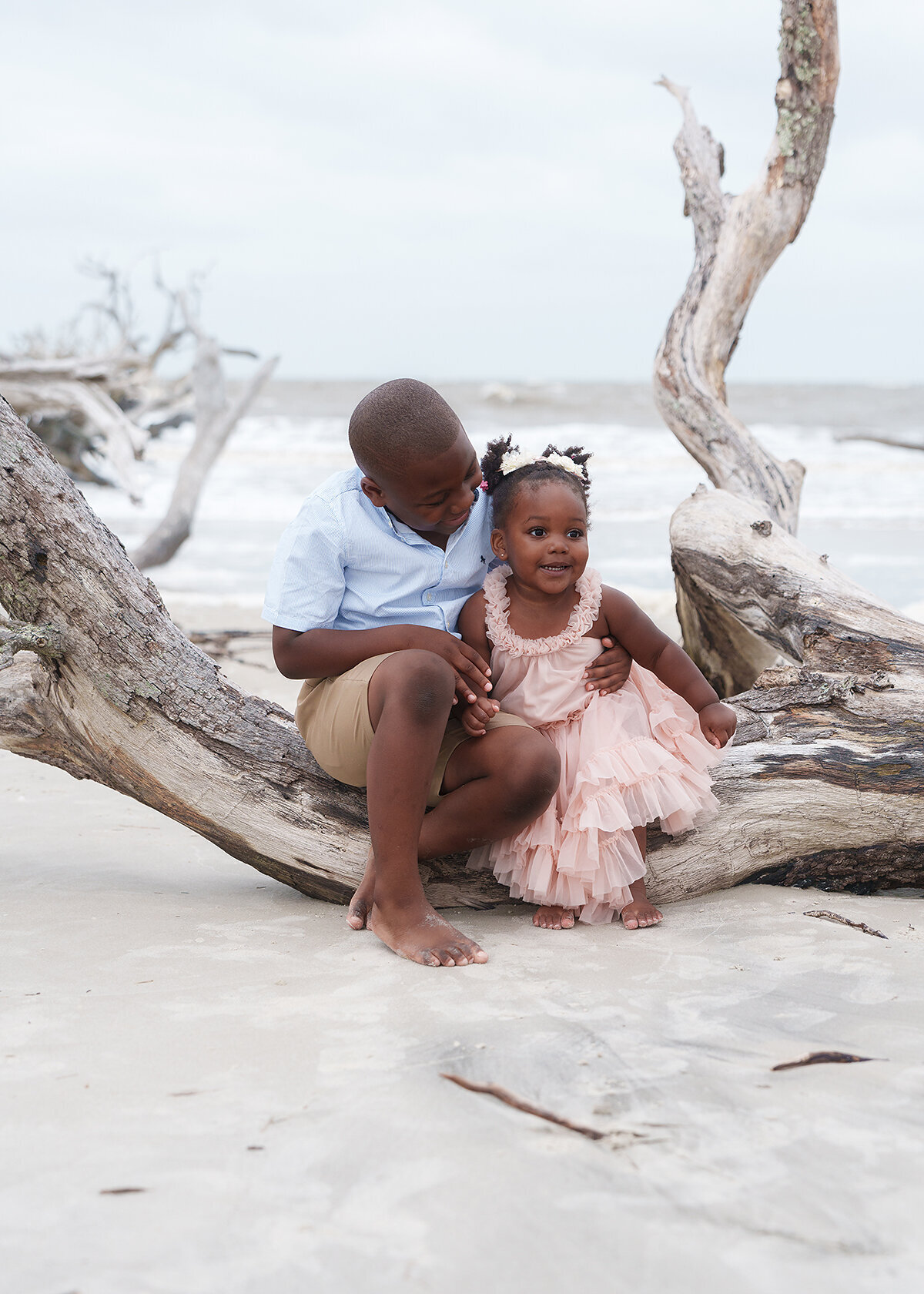 african american siblings photographed on jekyll island's famous driftwood beach at sunset on a stormy day