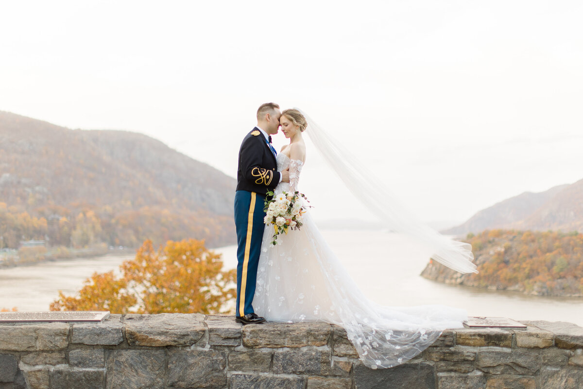 Groom in military uniform and bride posing in front of a river and mountain landscape