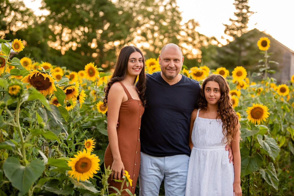 dad with his two teenage daughters in a sunflower field for their family photos in Burlington, On