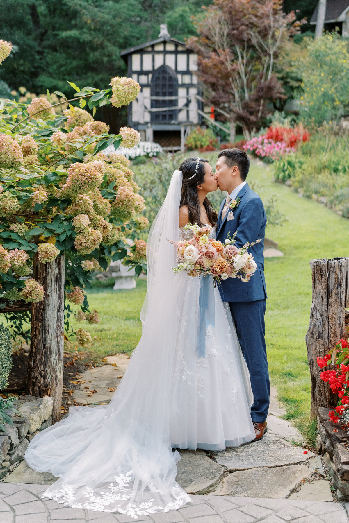 Bride and groom kissing in the garden pathway surrounded by hydrangeas at Castle Ladyhawke.