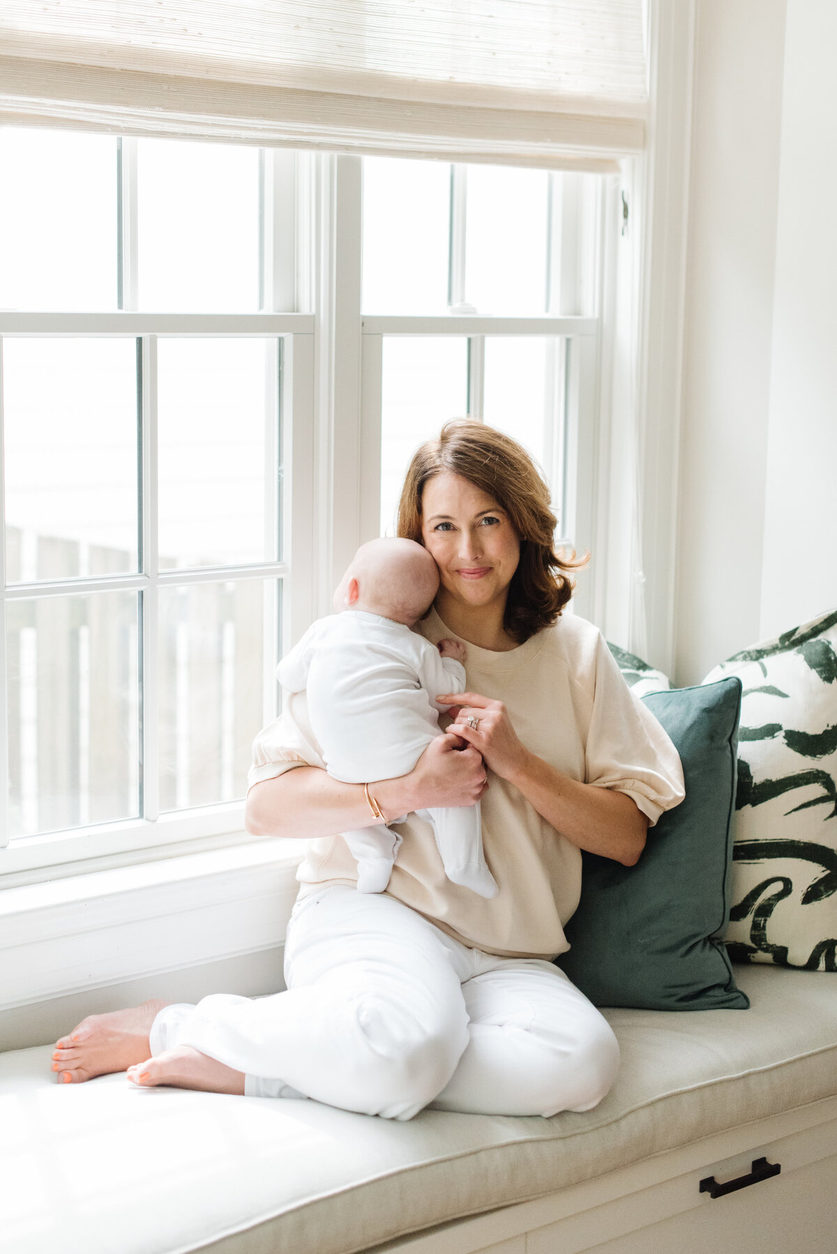 Mother holding baby on white windowsill in natural light