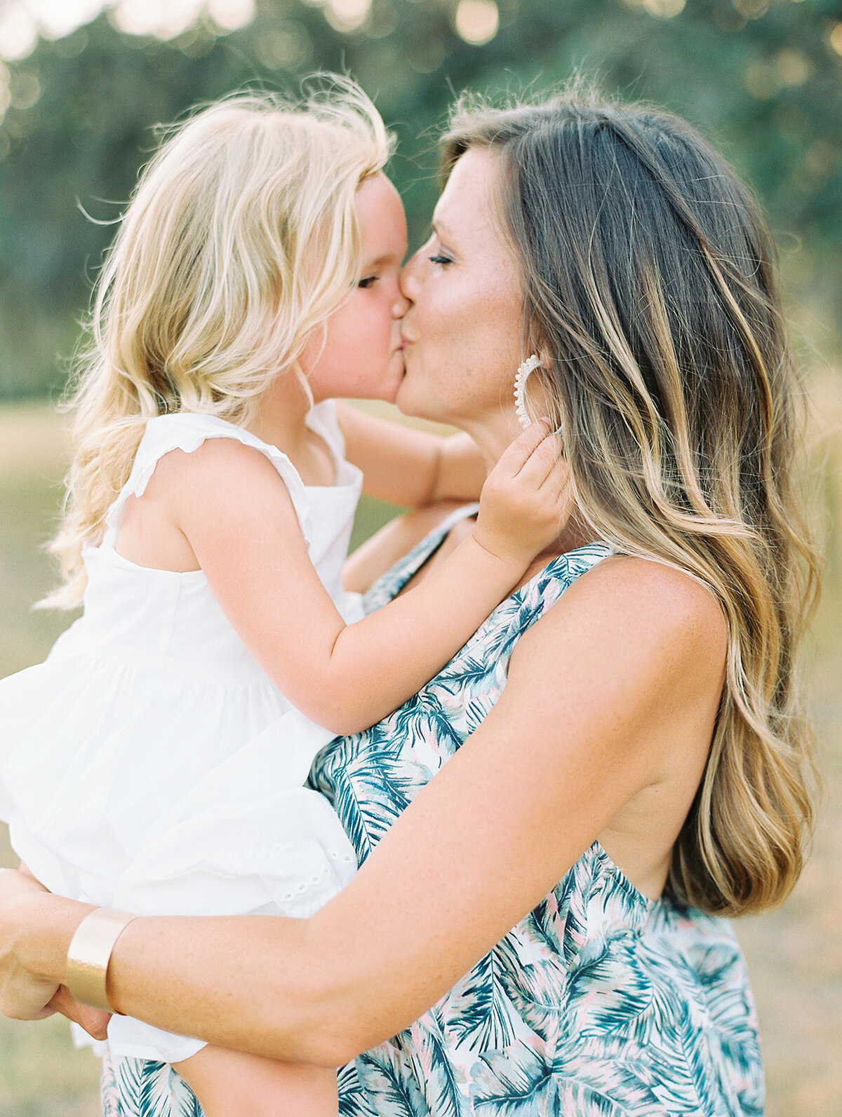 Mom in a patterned dress kissing her daughter in a white dress