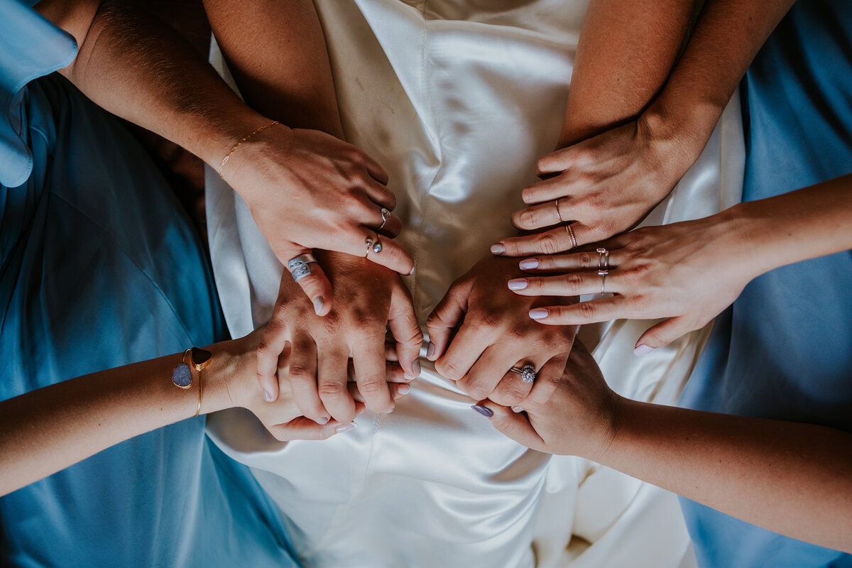 Camera looks down on bridesmaids hands as they pray over bride.