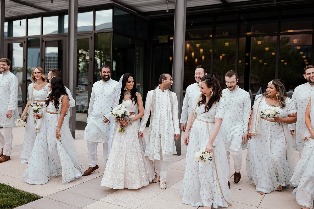 Indian Wedding Party wearing light blue sarees with gold accents and light blue sherwani with gold accents as they surround the Hindu bride and groom. The bride is wearing a white beaded saree with a light blue dupatta and the groom is wearing a white sherwani with a light blue dupatta at the Country Music Hall of Fame for their Nashville Wedding