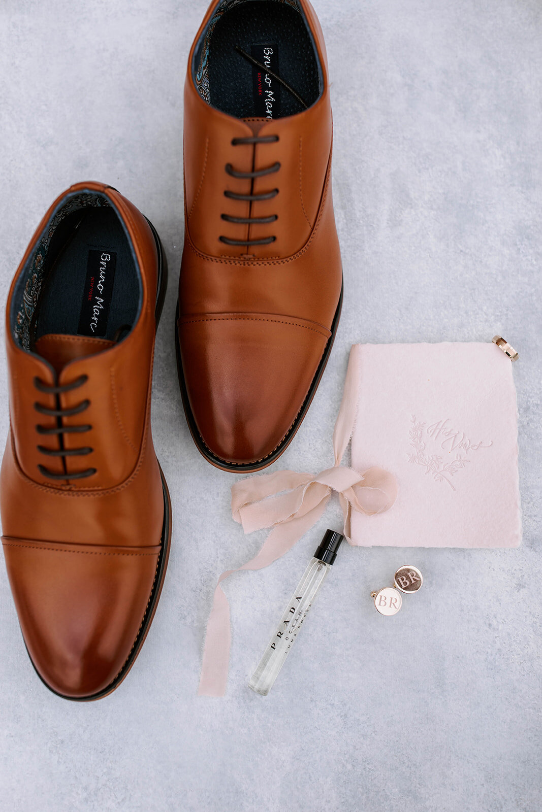 groom details flatlay photo with dress shoes, vow book and cologne
