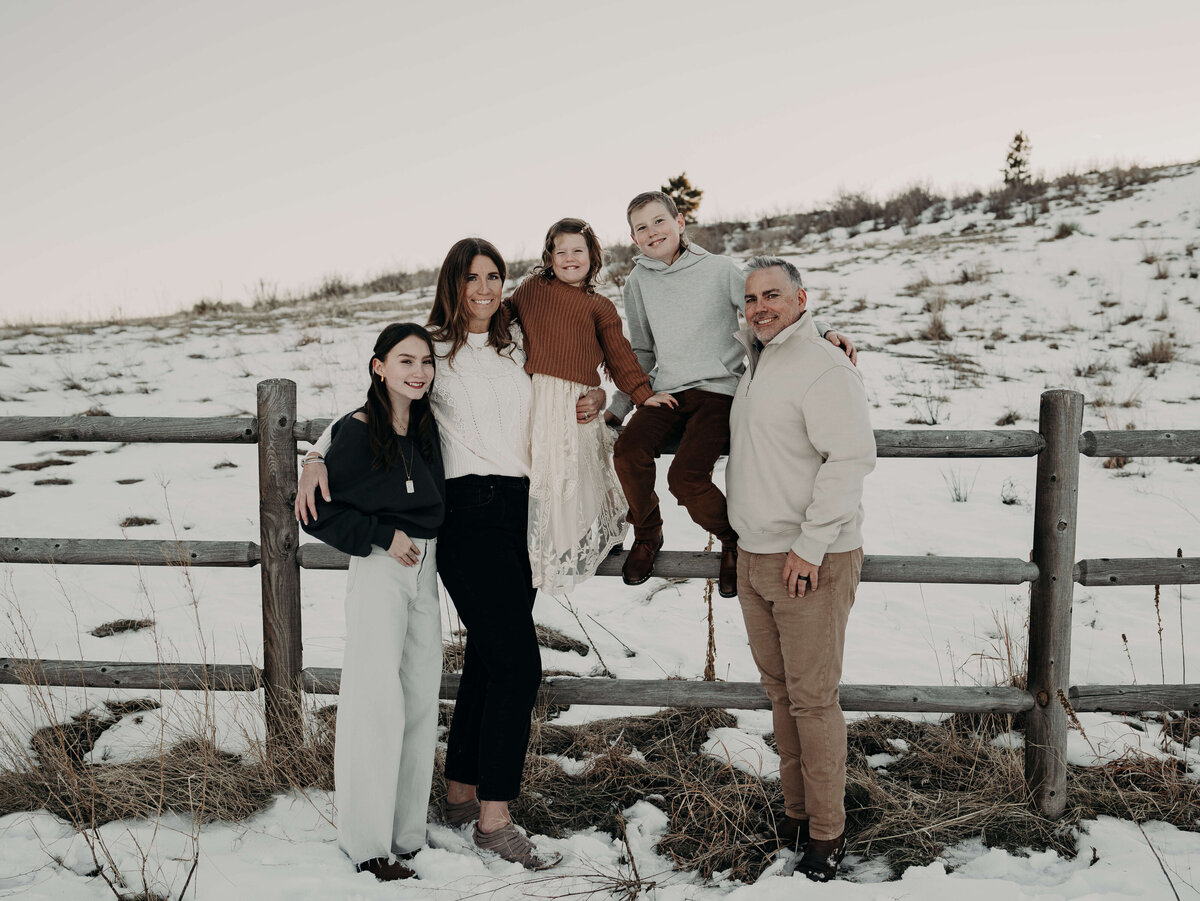 A family of five stylishly, dressed in winter cream, colored clothing poses organically along a fence on a Colorado farm just outside of Denver.