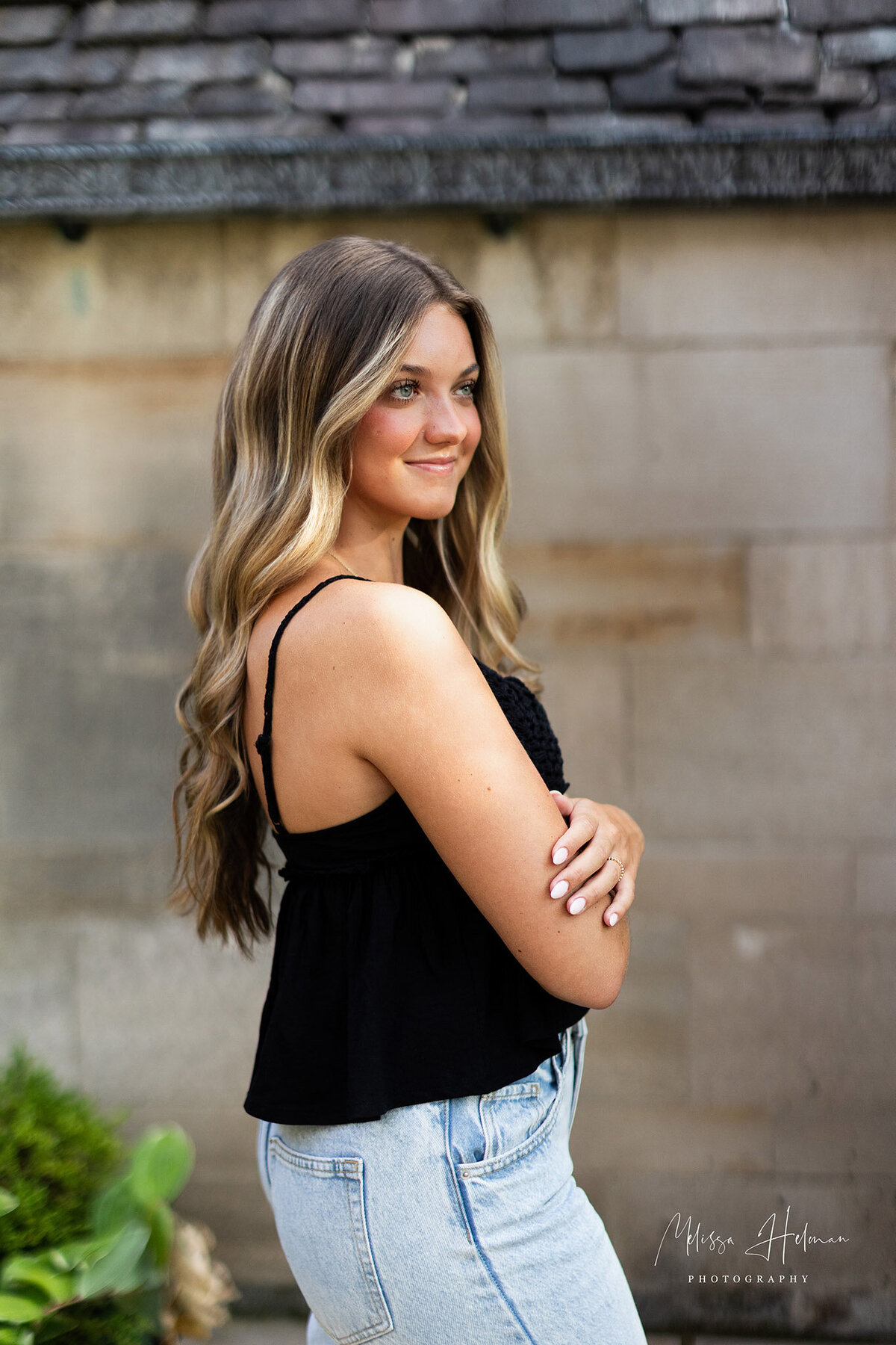 Highschool senior girl standing with a soft smile in black tank top with arms folded.