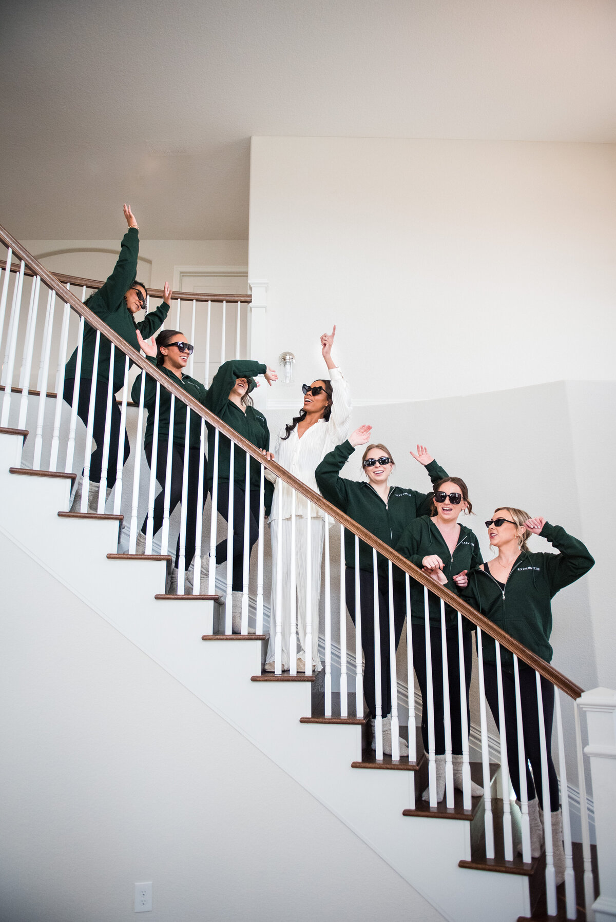A bride and her bridesmaids are dressed in pajamas and sunglasses, standing on a stairwell and making fun poses.