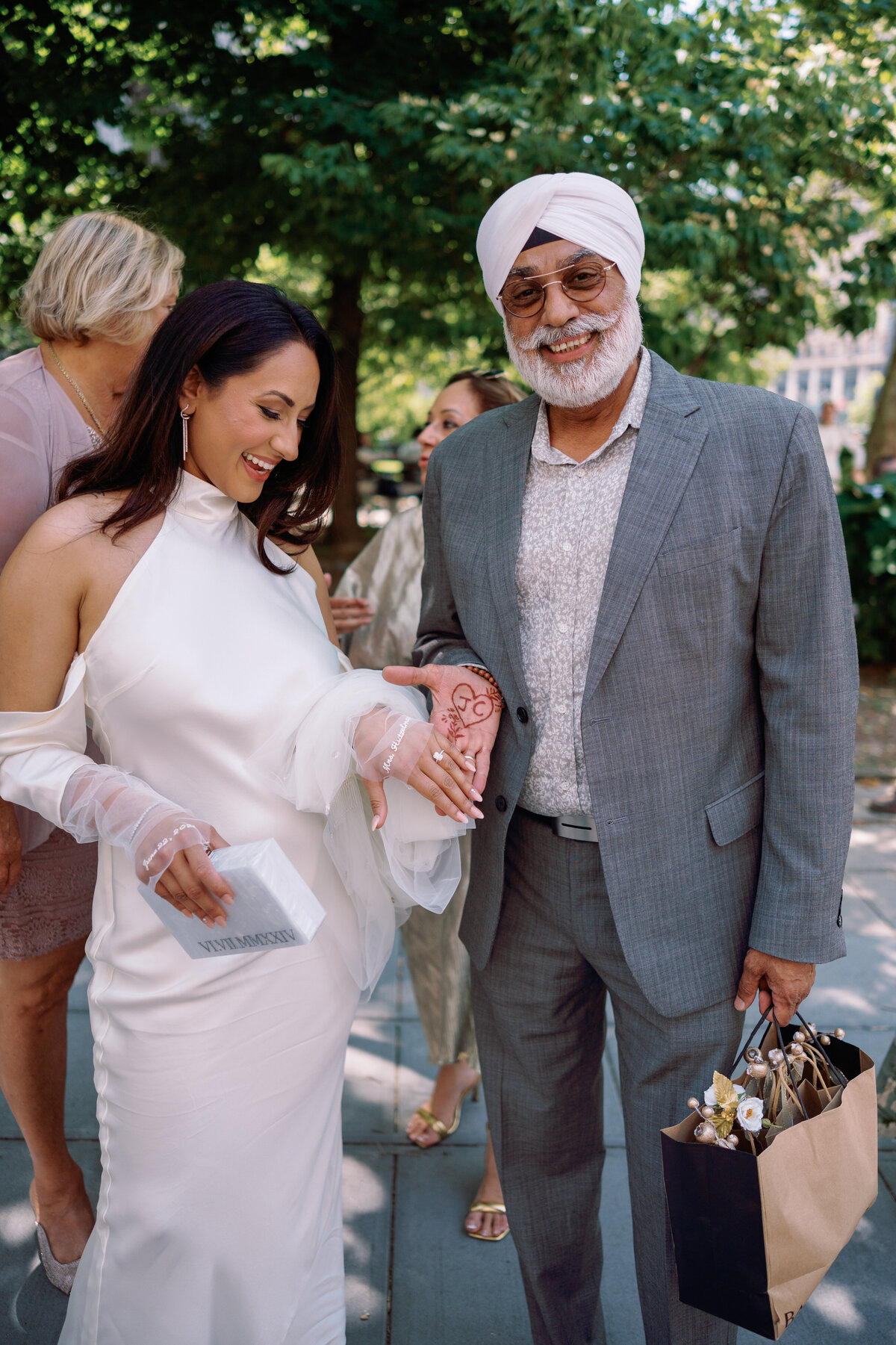 Bride smiling while holding her father’s hand outside New York City Hall, showing a henna design with initials “J + C,” captured during Japna and Chris’s intimate elopement by NYC wedding photographer Perry Hancock.