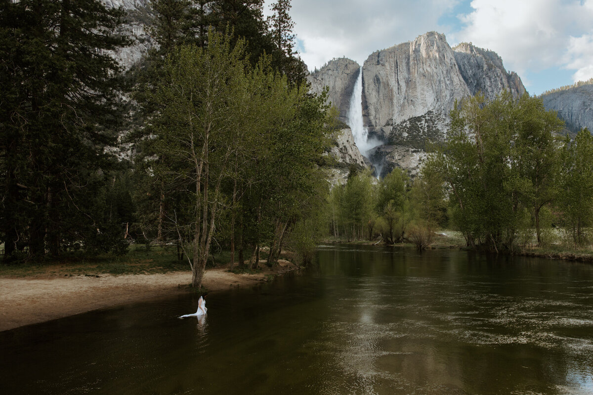 Carefree bride splashing in river in her wedding gown during Yosemite adventure elopement
