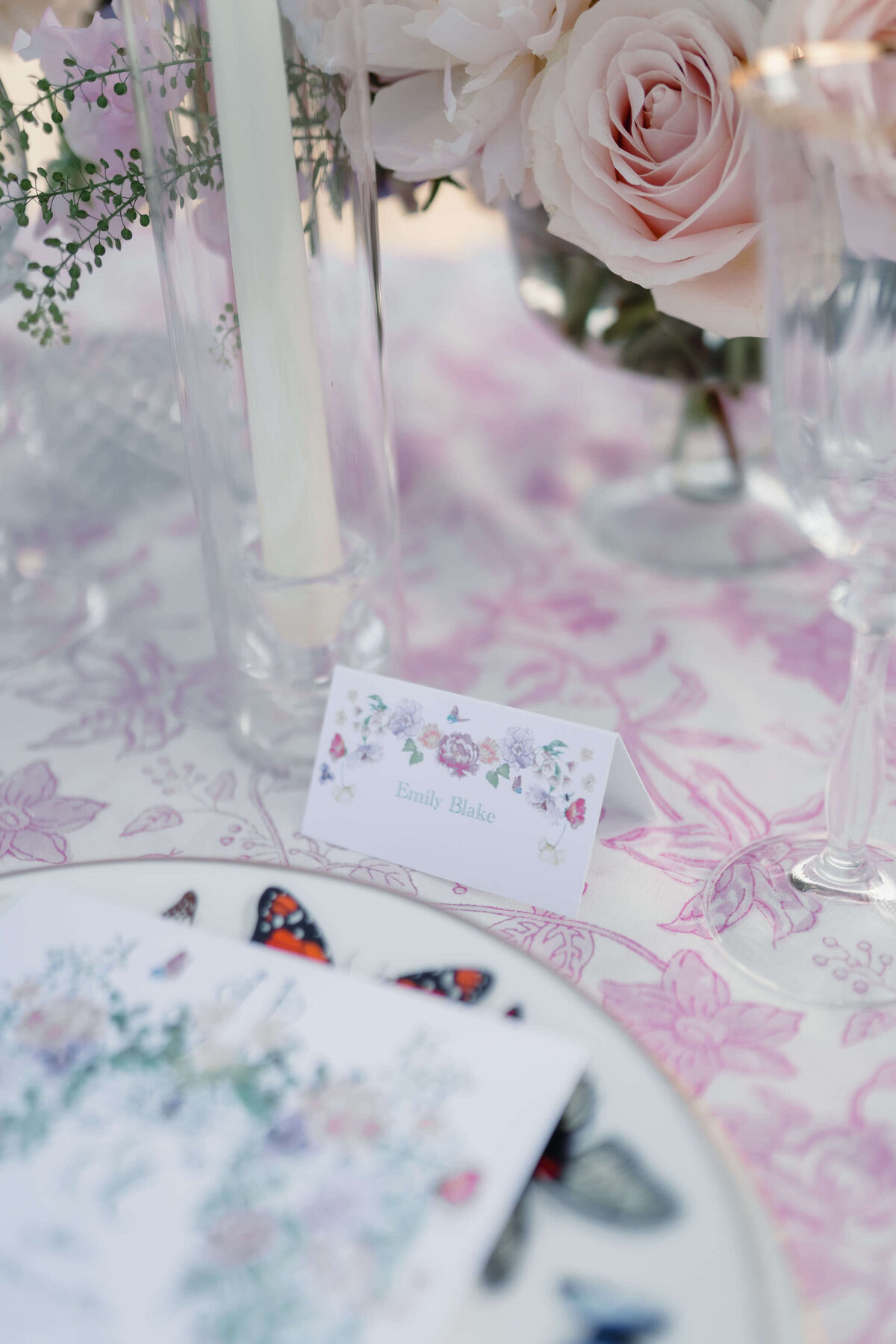 closeup of a wedding table design with pink and white floral linen and plates decorated with butterflies for a romantic garden wedding in the cotswolds