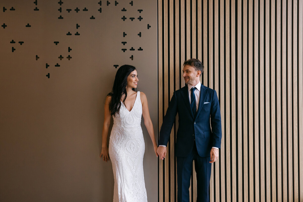 Brisbane Registry Office wedding couple holding hands and smiling in front of butterfly wall backdrop.