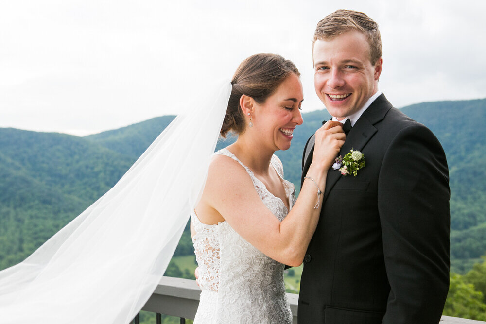 bride straightens the bowtie of the groom while he smiles at the camera