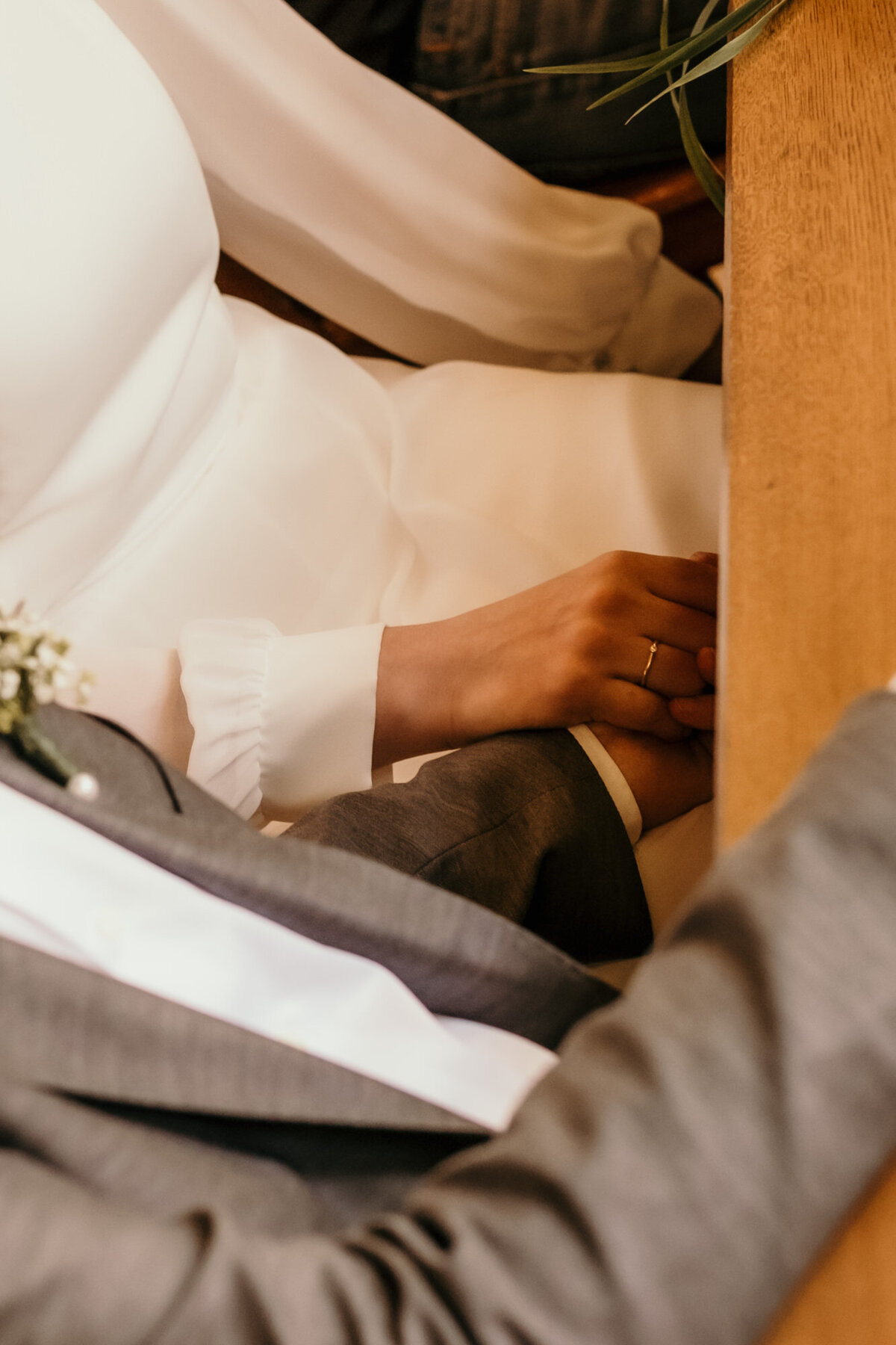 Während der standesamtlichen Trauung hält das Hochzeitspaar seine Hände unter dem Tisch verschränkt.