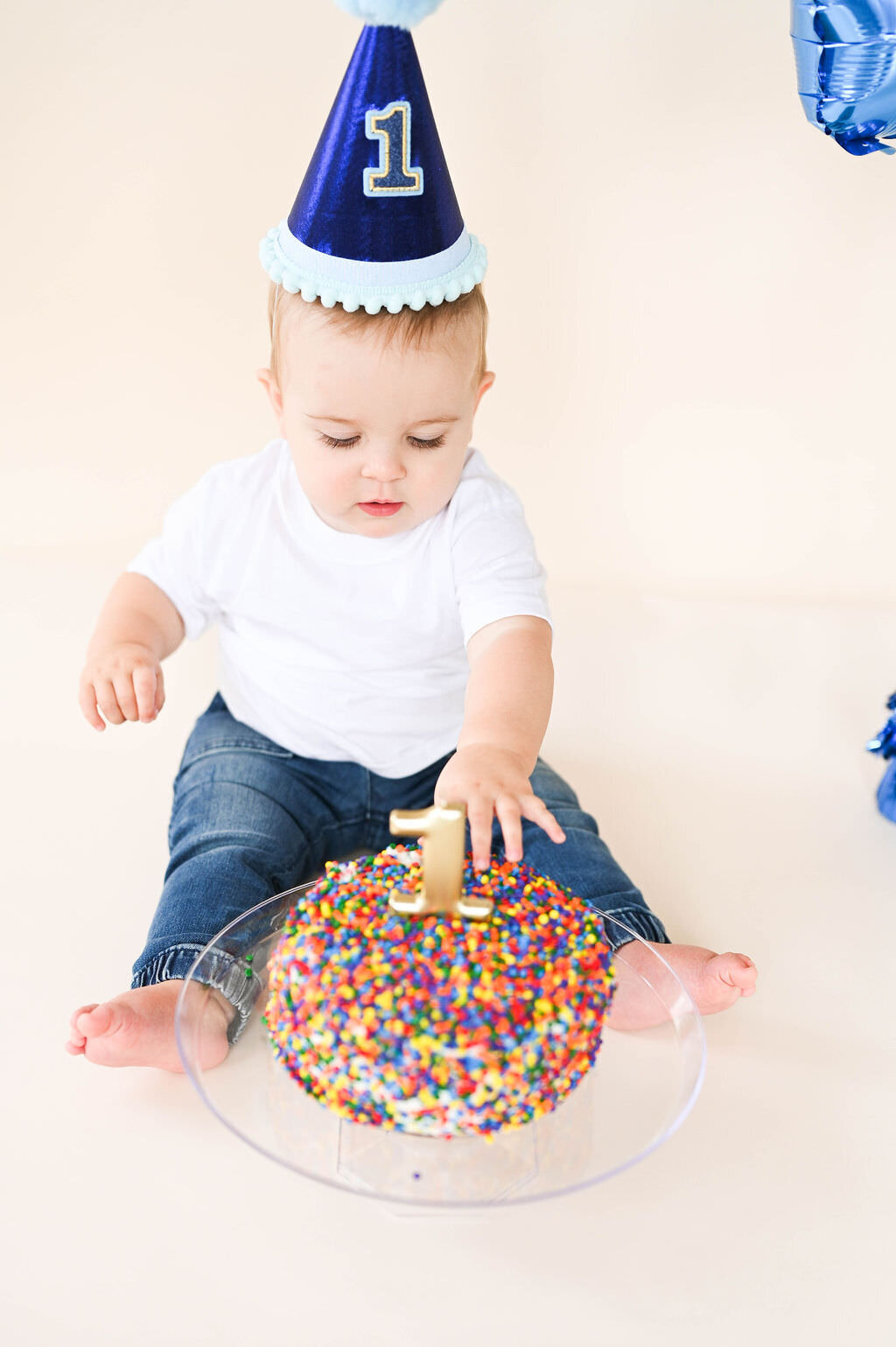 A small child with a party hat on reaching towards a round cake.