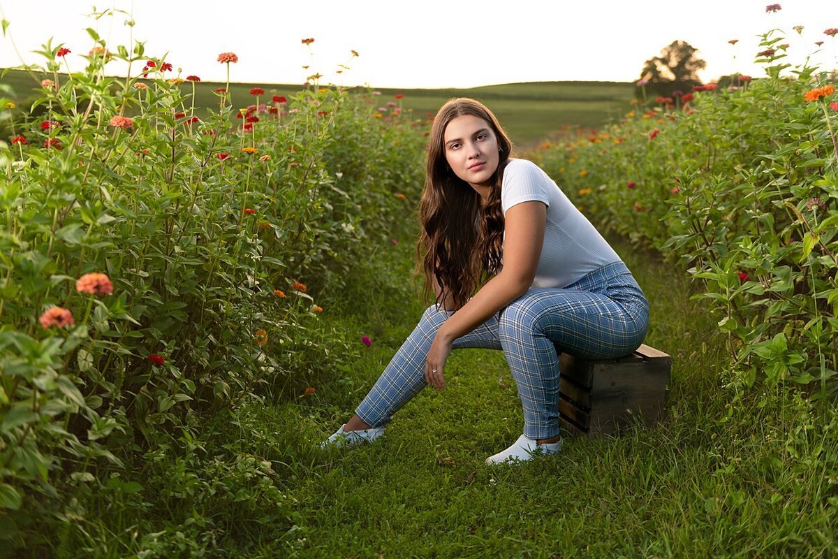 High school senior girl sitting on crate in field of flowers at Simmons Farm