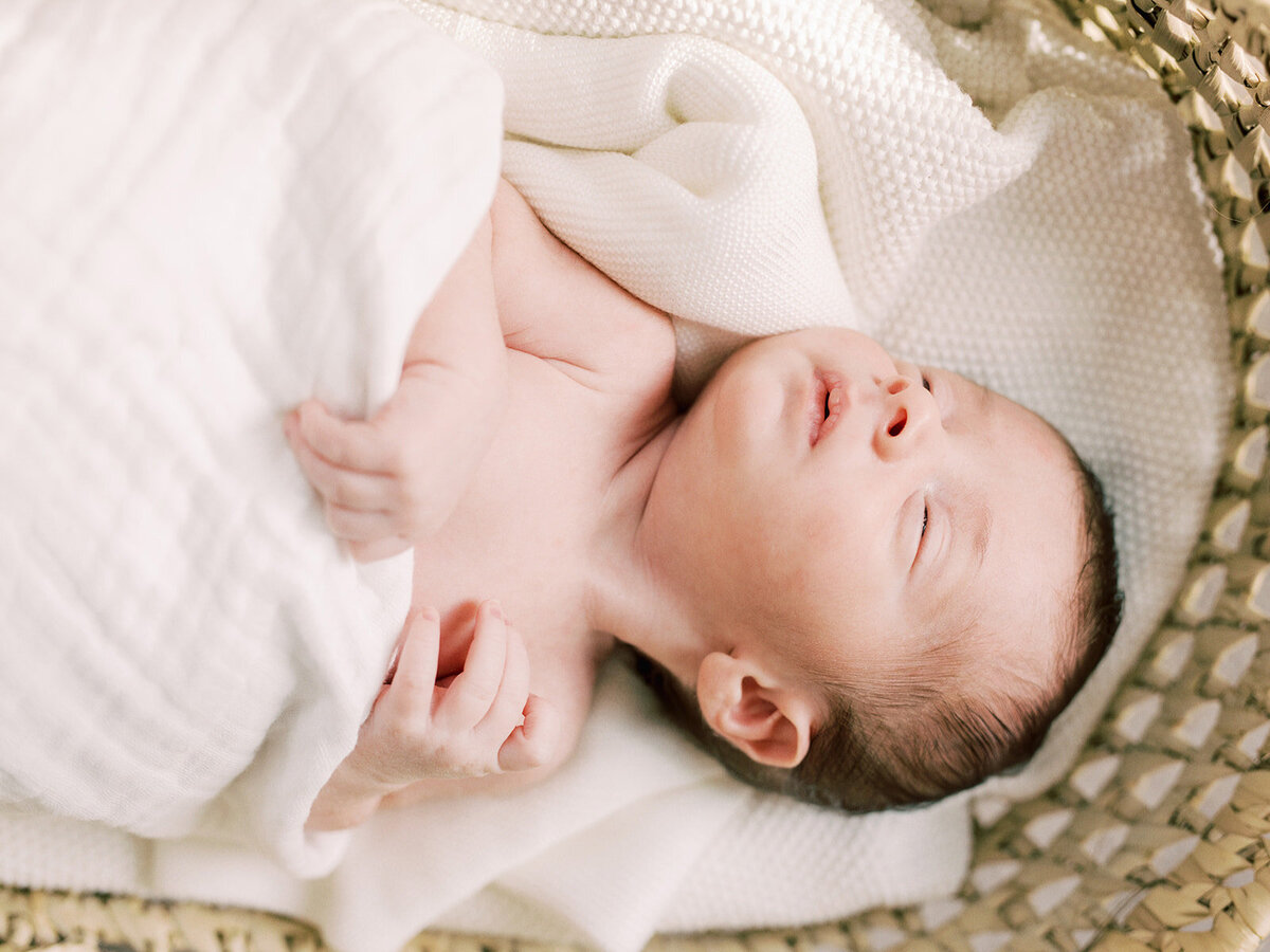 A baby sleeping in a basket while holding onto a blanket during a newborn photography session in Richmond by Katie Stansfield Photography.
