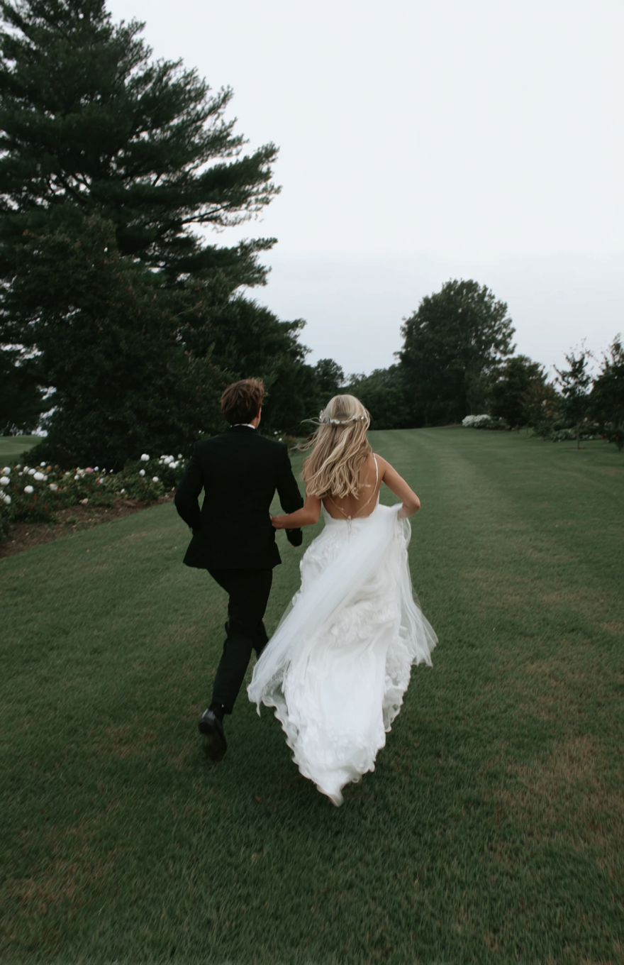 u8487914977_a_bride_and_groom_running_across_the_grass_at_the_a0305be1-7d23-45f1-a452-49ae18acff71_0