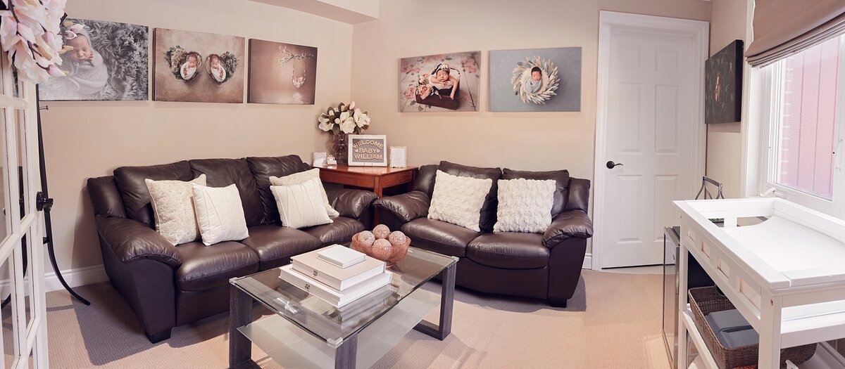 Cozy client lounge inside an Oakville newborn photography studio, featuring a leather sofa, neutral décor, and framed newborn artwork on the walls.