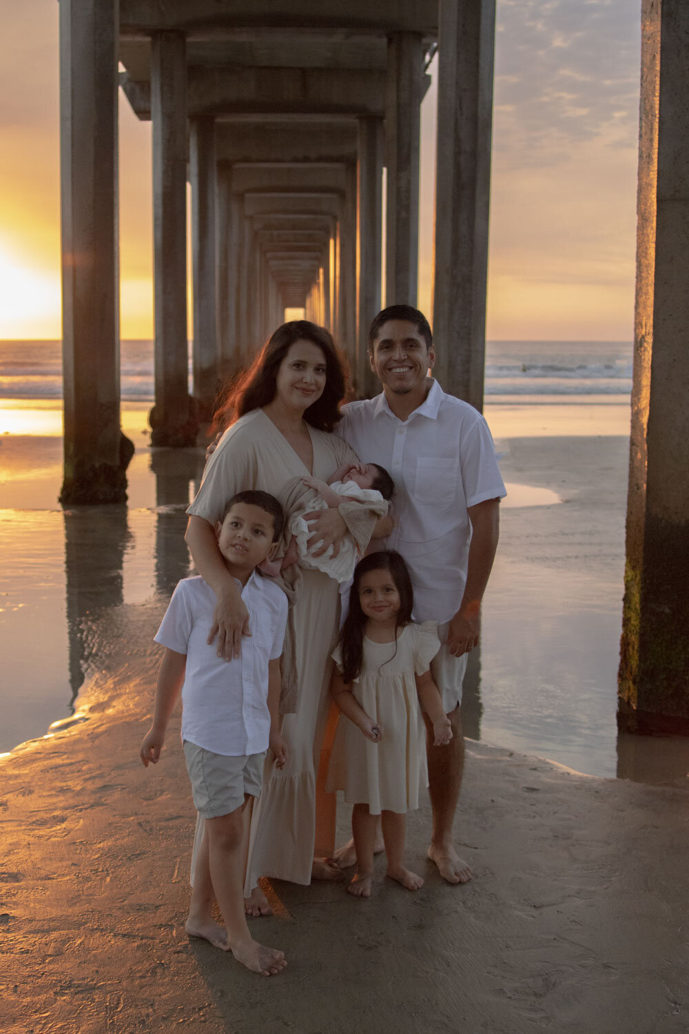 A family portrait under the pier at sunset, with parents and two children