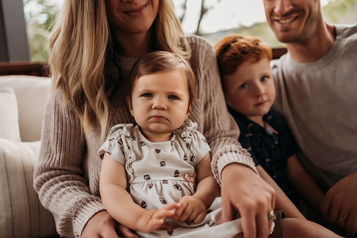 family of four sitting outside on patio while infant girl glares at the camera