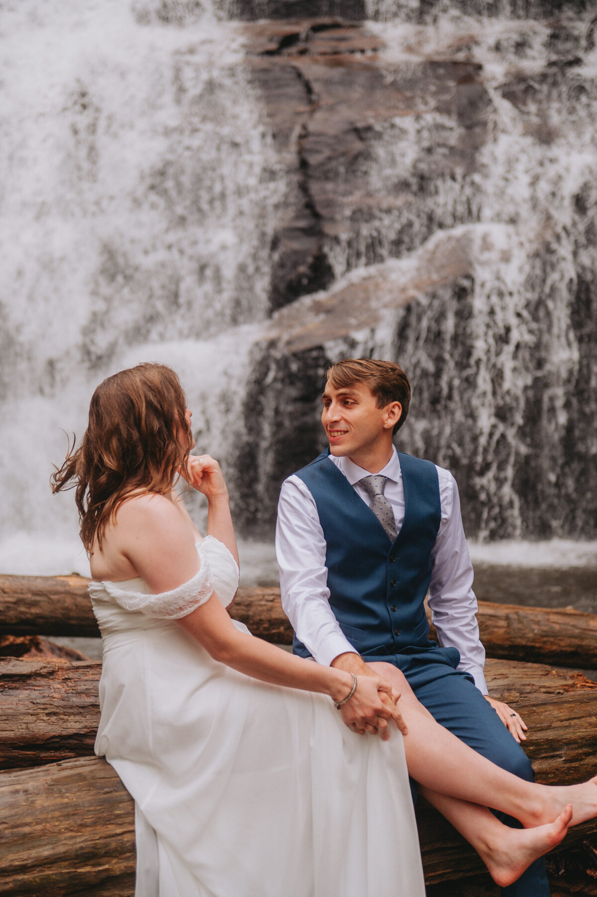 Newlyweds hold hands outdoors in front of a waterfall