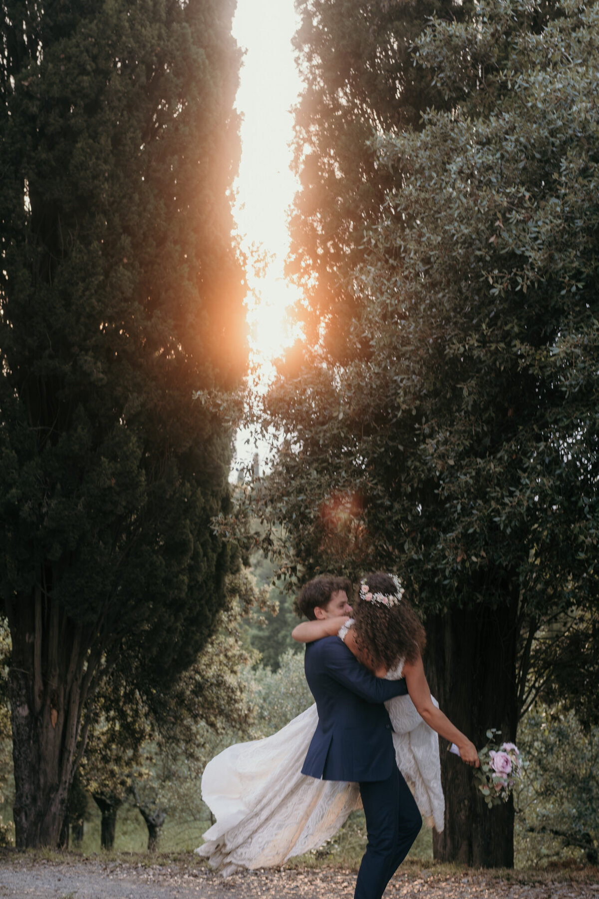 The groom is carrying his bride trhough a tree-lined path.