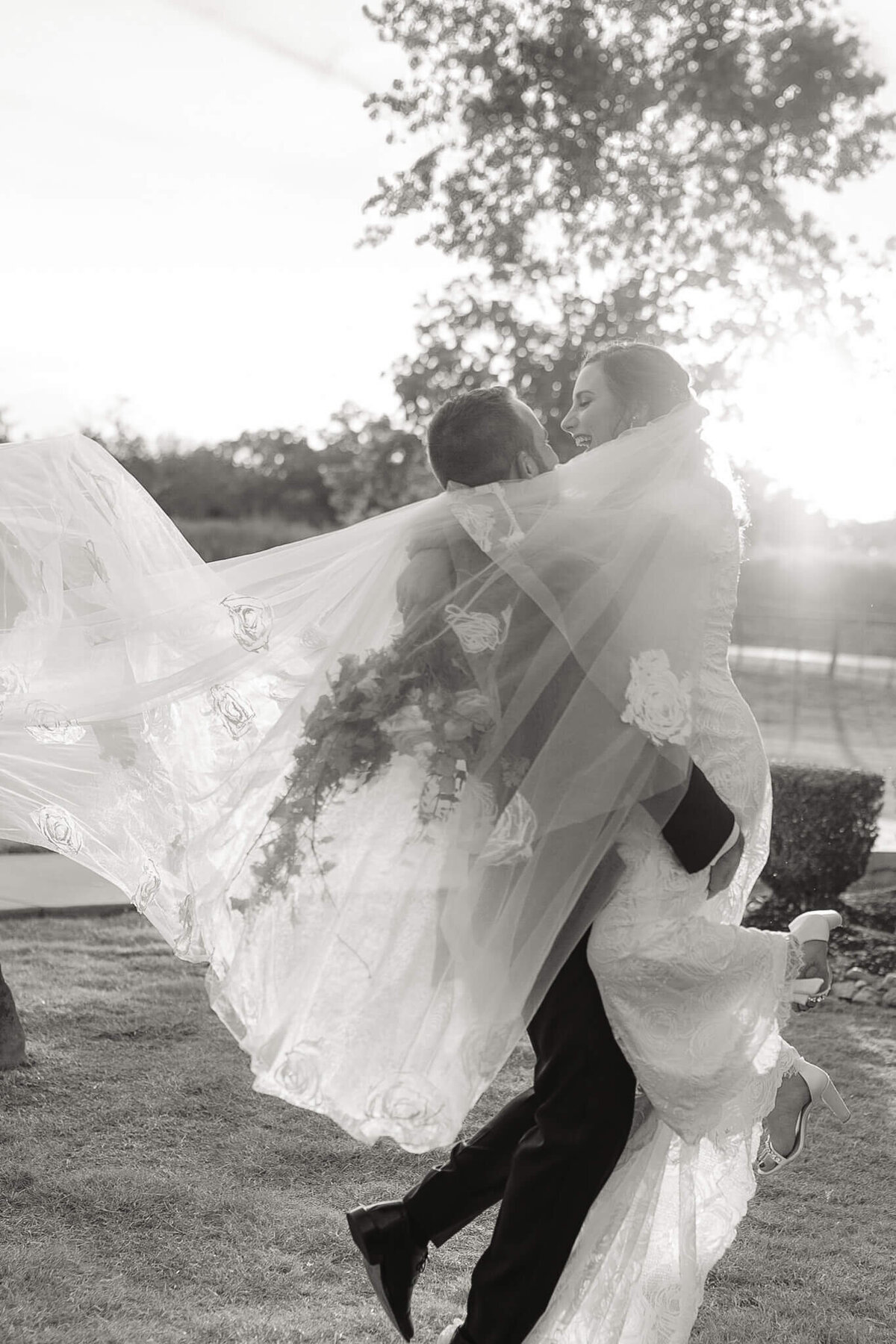 groom holding his bride and running with her as veil flows in the wind