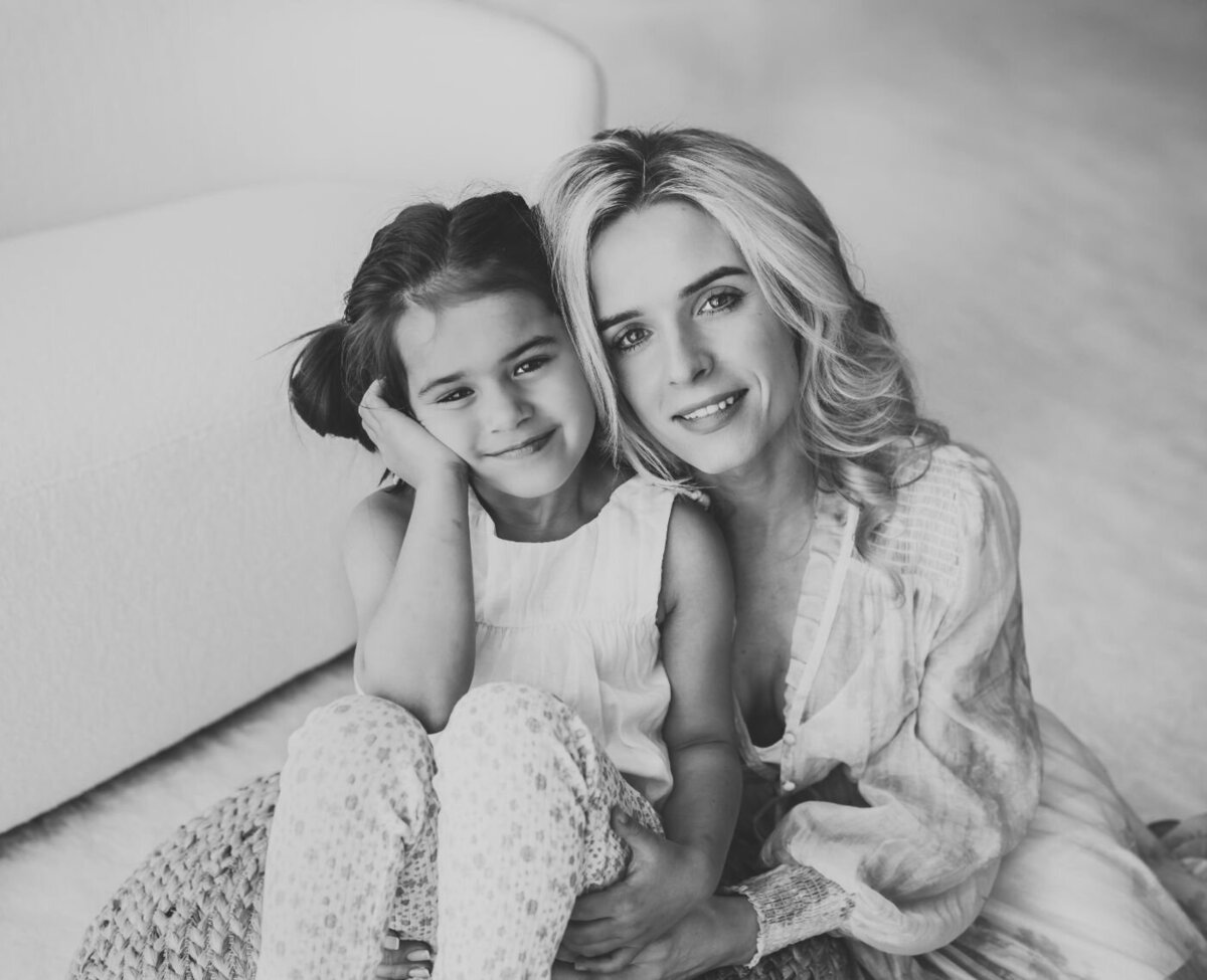 a mother and daughter sitting and smiling in a black and white photo